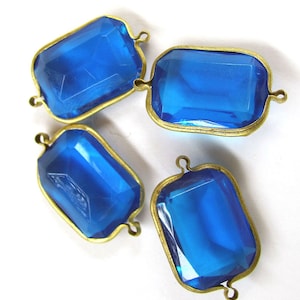 May include: Four blue glass rectangular-shaped beads with gold metal frames and loops. The beads are translucent and have a slight sparkle.