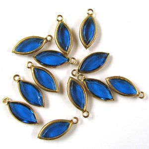 May include: Ten blue glass teardrop-shaped charms with gold-toned metal loops. The charms are arranged in a starburst pattern.