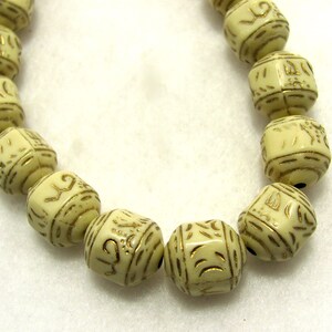 May include: A string of cream-colored beads with gold lettering. The beads are square-shaped and have intricate designs.