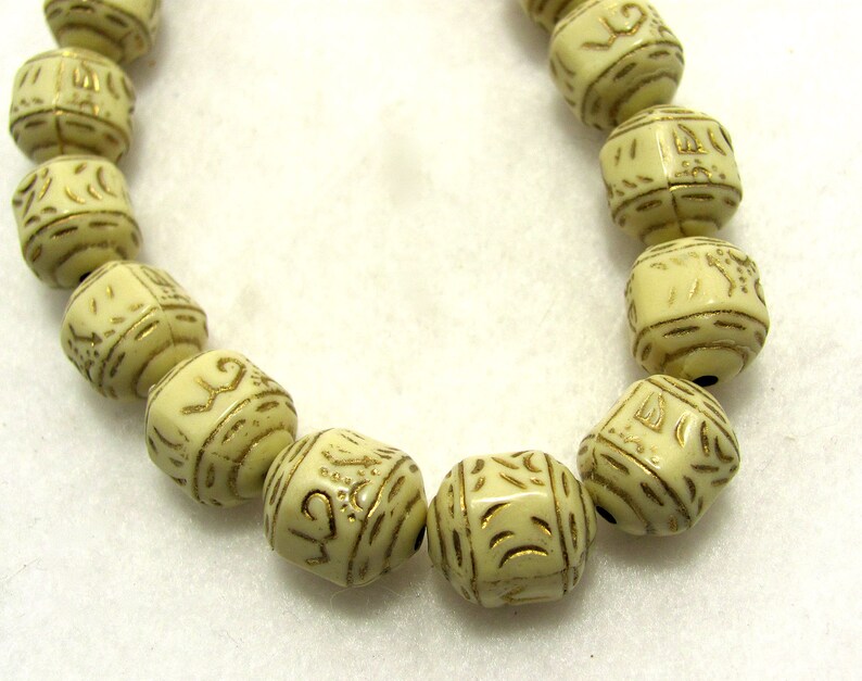May include: A string of cream-colored beads with gold lettering. The beads are square-shaped and have intricate designs.