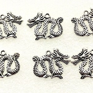 May include: Six silver-colored dragon charms. Each charm features a detailed dragon design with a loop at the top for attaching to jewelry or other crafts. The dragons are in a symmetrical pose.