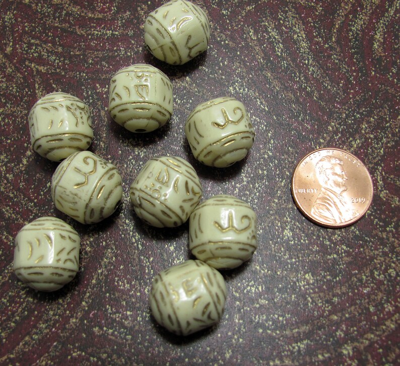 May include: Nine off-white ceramic beads with gold accents. Each bead has a different design. The beads are approximately the size of a US penny.