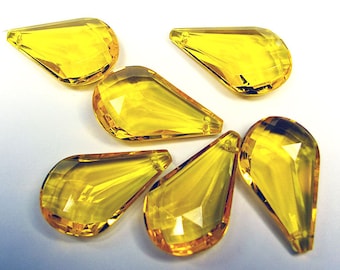 May include: Six faceted, teardrop-shaped yellow crystal beads. Each bead has a hole at the top for stringing. The beads are arranged on a white surface, showcasing their clarity and light refraction.