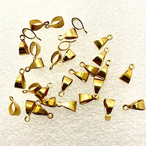May include: A collection of gold-colored pendant bails, ideal for jewelry making. The bails have a loop at the top for attaching to a chain or cord and a flat base for gluing or attaching to a pendant. The bails are made of a shiny, metallic material.