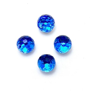 Op de afbeelding: Vier gefacetteerde blauwe kristallen kralen op een witte achtergrond. De kralen hebben een bolvorm en een geometrisch patroon van kleine, platte oppervlakken die het licht reflecteren. De kleur gaat over van een diepblauw naar een lichter, helderder blauw.