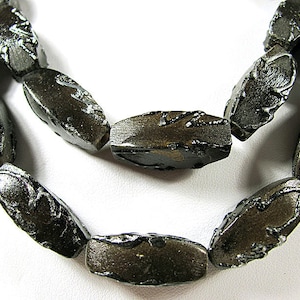 May include: A strand of dark gray oval-shaped beads with a textured surface. The beads are made of glass and have a metallic finish.