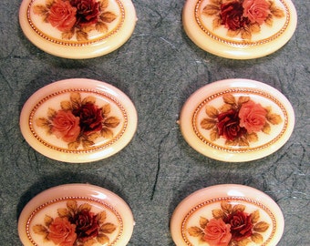 May include: Six oval-shaped buttons with a cream-colored background and a gold trim. Each button features a floral design with pink and red roses.