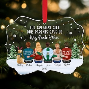 May include: A clear acrylic Christmas ornament with a red ribbon. The ornament features a family illustration with the text "THE GREATEST GIFT OUR PARENTS GAVE US Was Each Other" and names. A dog is also included. The year 2025 is printed at the bottom.