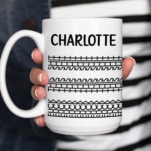 May include: White ceramic mug with a black and white geometric design and the name "CHARLOTTE" printed on the front.
