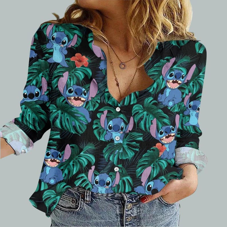 May include: A long-sleeved button-down shirt featuring a repeating pattern of the character Stitch from Lilo & Stitch. The design includes blue Stitch figures, green tropical leaves, and red flowers on a black background. The shirt has a V-neck and button closure.