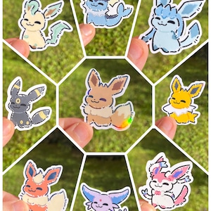 Op de afbeelding: Een verzameling van acht kleurrijke cartoonstickers met verschillende Eevee-evoluties. Elke sticker toont een ander ontwerp met unieke kleurenpaletten, waaronder blauw, geel, roze en zwart, met witte contouren. De stickers worden tegen een groene, grasrijke achtergrond gehouden.