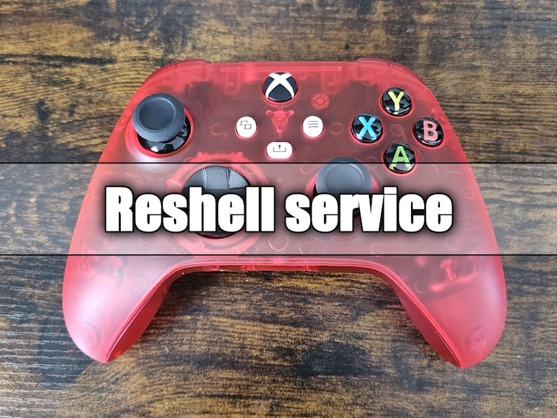 May include: A transparent red Xbox controller with black thumbsticks and colored buttons. The text "Reshell service" is overlaid on the controller. The controller is on a wooden surface.