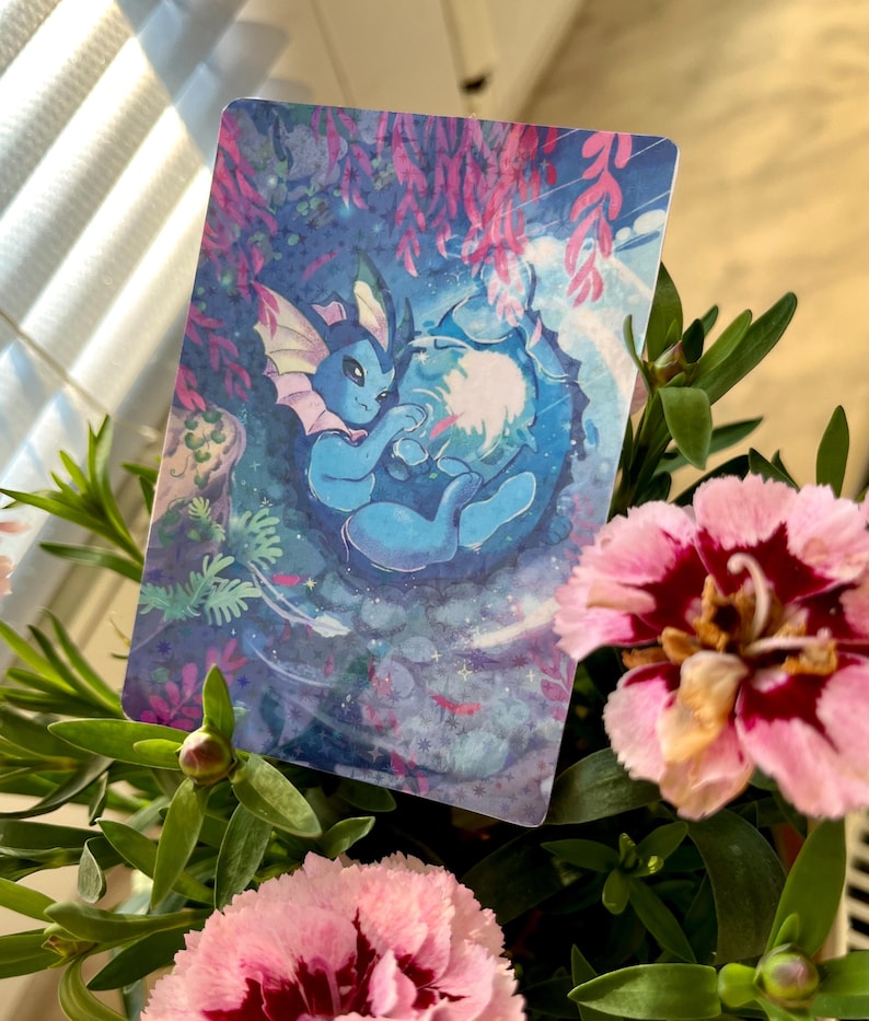 May include: A rectangular card featuring a blue cartoon creature with pink accents, set against a blue and purple underwater scene. The card is surrounded by pink and red flowers and green foliage.