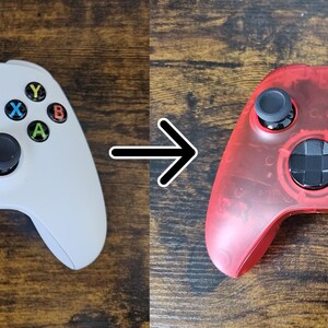May include: An Xbox controller in white and a transparent red. The white controller has black joysticks and buttons with colored letters. The red controller has black joysticks and buttons with colored letters. The controllers are on a wooden surface.