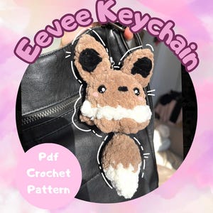 May include: A handmade Eevee keychain made of brown and white yarn, with black accents. The keychain is attached to a black bag. Text on the image reads "Eevee Keychain" and "Pdf Crochet Pattern".