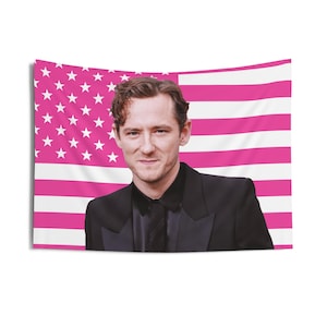 Könnte beinhalten: Eine rechteckige Wandtapete mit einem Porträt eines Mannes in einem schwarzen Anzug vor einem rosa und weißen amerikanischen Flaggen-Design. Geeignet für die Wanddekoration.