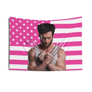 Puede incluir: Un tapiz de pared con un diseño de bandera estadounidense rosa y blanca con un retrato de un hombre con garras de metal. El hombre lleva una camiseta sin mangas blanca y tiene una expresión severa.