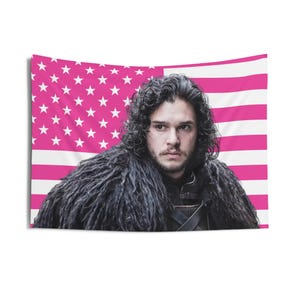 Puede incluir: Un tapiz rectangular con un hombre de pelo rizado oscuro y una capa forrada de piel. El fondo es un diseño de bandera estadounidense rosa y blanca. El tapiz es probablemente de tela.