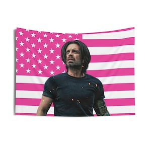 Peut inclure: Une tapisserie représentant un homme en t-shirt noir devant un drapeau américain rose et blanc. Le drapeau présente des étoiles blanches sur un champ rose et des rayures roses et blanches. L'homme a les cheveux longs et foncés et une expression sérieuse.