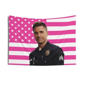 May include: A pink and white American flag tapestry with a portrait of a man in a police uniform. The man is smiling and the flag has white stars and pink stripes. The tapestry is rectangular and hangs against a white background.