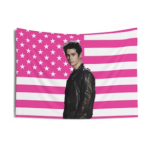 May include: A pink and white American flag tapestry with a portrait of a person wearing a black leather jacket. The flag design features white stars on a pink background and pink and white stripes.