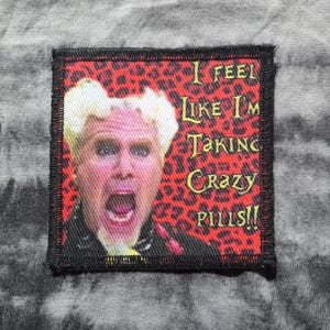 May include: Square patch with a black border featuring a portrait of a person with blonde hair and an open mouth, set against a red leopard print background. Text reads "I FEEL LIKE I'M TAKING CRAZY PILLS!!".