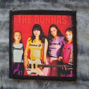 May include: Square patch with a band photo and the text "THE DONNAS" on a red background. The image shows four women, one holding a white bass guitar. The women are wearing different coloured shirts with text on them. The patch has a black border.