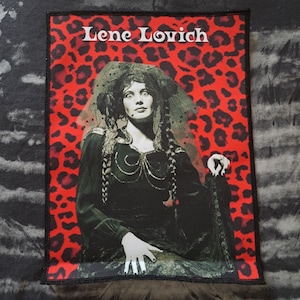 May include: A rectangular patch featuring a portrait of Lene Lovich against a red leopard print background. The text "Lene Lovich" is displayed in white at the top. The portrait is a black and white image of a woman with long braids and a veil.