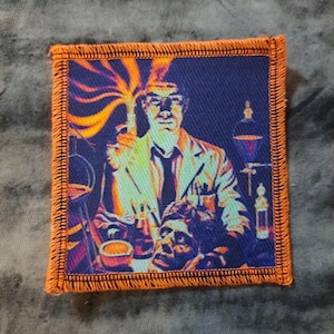 May include: Square patch with an orange border featuring a scientist in a lab coat holding a flask with a fiery explosion. The image has a blue background with lab equipment and a sculpted head.