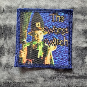 Peut inclure: Écusson carré à bordure bleue représentant une sorcière tenant un balai. Le texte "The Worst Witch" est brodé dans une police fantaisiste. Le fond est un motif bleu.