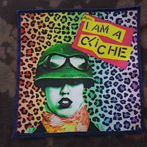 May include: Square patch with a pop art design. The patch features a person wearing a green helmet and goggles, with the text "I AM A KICHE" in yellow and pink. The background has a leopard print pattern in rainbow colors.