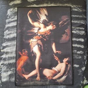 May include: A rectangular patch featuring a classical painting of a winged figure with two other figures. The artwork is rendered in a dark color palette with highlights of skin tones and metallic accents. The patch has a black border.