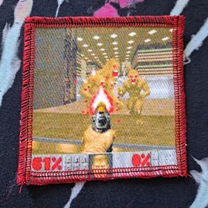 May include: Square patch with a red border featuring a pixelated scene from a video game. The scene depicts a character shooting at several yellow monsters with a fiery weapon. The patch has a health bar at the bottom.