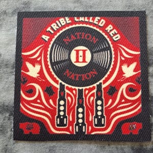 May include: Square patch with a red and black design. The patch features the text "A Tribe Called Red" around a central circular graphic of a record. The word "Nation" is also visible. Decorative elements include stylized birds and geometric shapes.