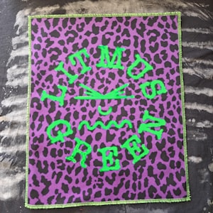 May include: Square patch with a purple leopard print background and green text that reads "IT MUST BE FREE". The patch has a green border.