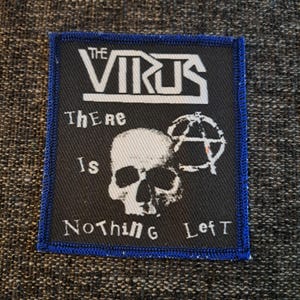 May include: A rectangular black fabric patch with a blue stitched border. It features the white text THE VIRUS at the top, a central white skull graphic next to an anarchy symbol, and the white text There Is Nothing LefT below the skull.