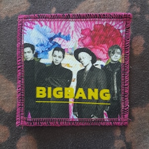 May include: Square patch with a pink border featuring a group of four people in black clothing against a floral background of pink, blue, and white. The word "BIGBANG" is in yellow block letters.