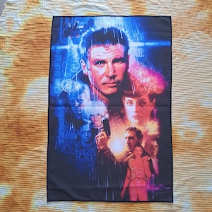 May include: A black rectangular poster featuring a movie poster design with several faces and text. The poster has a blue and red color scheme, with the main face being a man with short hair. The poster is on a yellow and orange patterned surface.