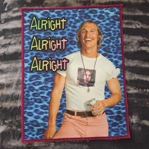 May include: Rectangular patch with a smiling man in a white t-shirt and pink trousers, holding a can. The background is blue with a leopard print. The words "Alright Alright Alright" are stacked vertically in colourful letters.