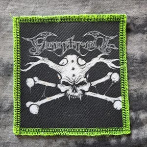 Puede incluir: Una taza de cerámica blanca con asa negra y el texto "But First, Coffee" en negrita negra. La taza se encuentra sobre un fondo borroso, sugiriendo un ambiente acogedor.