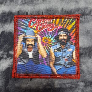 May include: A rectangular patch with a red border featuring a colorful image of two men. The image has a tie-dye background and the words "Cheech & Chong" in a stylized font. The men are wearing hats and denim.