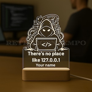 Peut inclure: Lampe de bureau en acrylique éclairée avec une base en bois. La lampe présente un design de hacker avec une figure encapuchonnée et un ordinateur portable, avec le texte "There's no place like 127.0.0.1 Your name".
