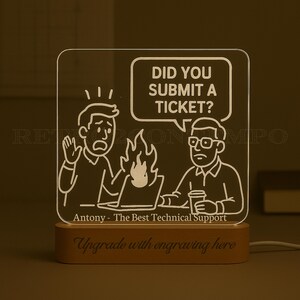 Peut inclure: Lampe LED rectangulaire avec une base en bois. Elle présente une illustration de dessin animé avec le texte "DID YOU SUBMIT A TICKET ?" et "Antony - The Best Technical Support". La base indique "Upgrade with engraving here".