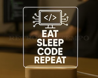 May include: A rectangular LED desk lamp with a wooden base. The lamp features a white graphic of a computer monitor with code symbols and the words "EAT SLEEP CODE REPEAT" in a bold, sans-serif font. The lamp is lit, and the background is blurred.
