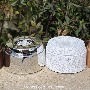 May include: Four aromatherapy oil diffusers in a row. The diffusers are made of different materials, including wood and metal. The colors are brown, silver, white, and light brown. The diffusers are sitting on a stone surface.