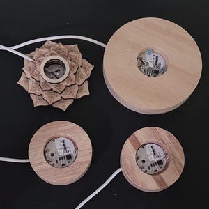 May include: Four wooden bases with a circular cutout in the center. Each base has a small circuit board with LED lights inside. The bases are different sizes and are arranged in a grid pattern.