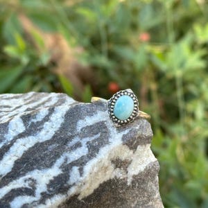May include: A silver ring with a light blue oval gemstone set in a beaded bezel.