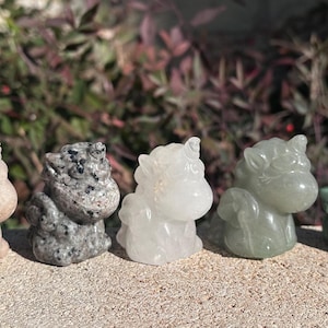 May include: Five small unicorn figurines carved from different types of stone. The unicorns are in a row from left to right: light pink, gray and white speckled, white, light green, and dark green.