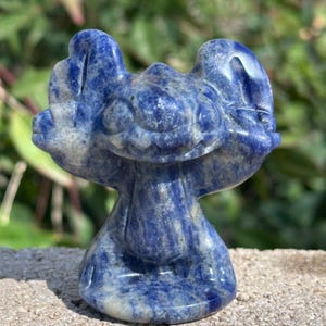 May include: A blue and white carved lapis lazuli figurine of Stitch from the Disney movie Lilo & Stitch.