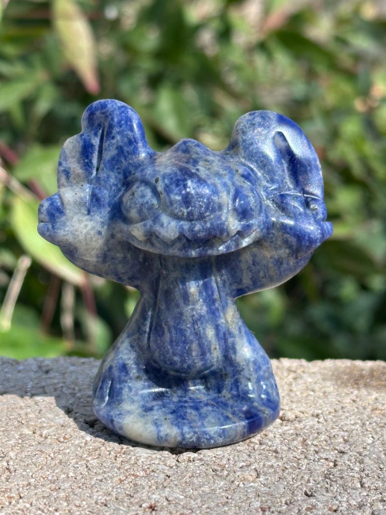 May include: A blue and white carved lapis lazuli figurine of Stitch from the Disney movie Lilo & Stitch.